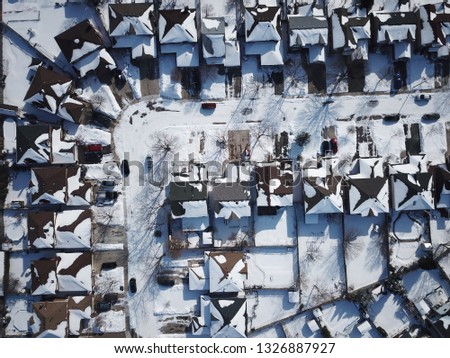 Aerial drone photo, top down, of suburban houses in Canada everything is white and covered with snow in the sunshine.