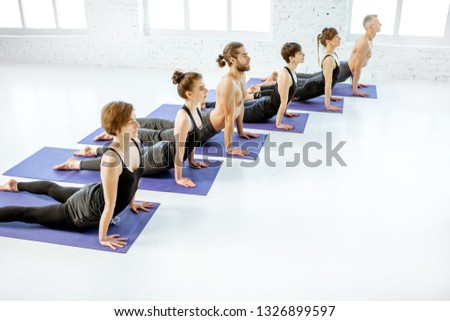 Young group of people practising yoga, keeping pose arranged together in a row in the white spacious studio