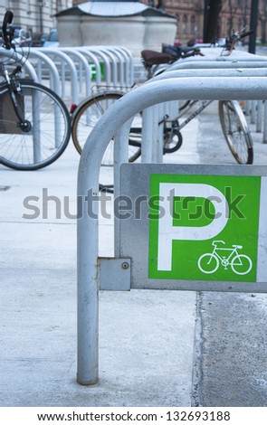 Urban bicycle parking railings with a green parking sign and a few bicycles in the background