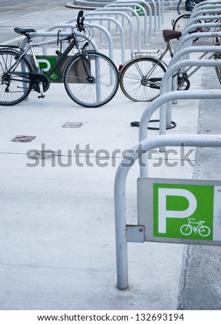 Urban bicycle parking railings with a green parking sign and a few bicycles in the background