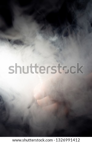 Male hand holds vape in thick vape fog or smoke. Vape clouds around hand with vape on black background. Fog is white. Stock isolated white smoke.