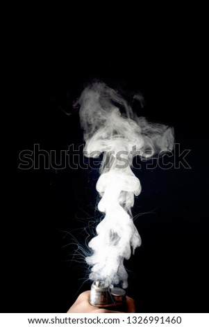 Male hand holds vape without atomiser. Column of vape clouds splash from coil on black background. Fog is white. Stock isolated white smoke with spray boiling glycerine.