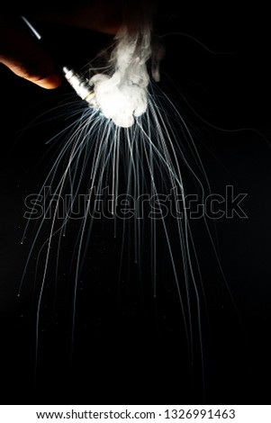 Male hand holds vape upside down. Vape clouds splash from coil on black background. Fog is white. Stock isolated white smoke with spray boiling glycerine.