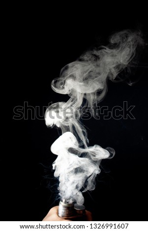 Male hand holds vape without atomiser. Column of vape clouds splash from coil on black background. Fog is white. Stock isolated white smoke with spray boiling glycerine.