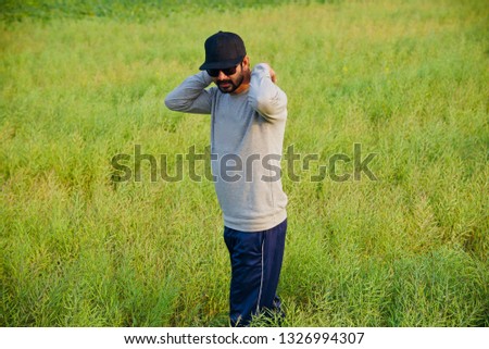 Young man wearing a cap and sunglasses standing in a green crops field