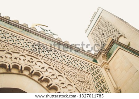 Exterior of the Grand Mosque of Paris featuring carved geometric shapes, ornamental details, green marble tiling and arabic writing.