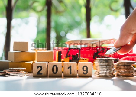 Hand put coins on transportation vehicle and wooden block 2019 background using as logistic and shipping concept