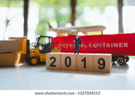Miniature people, businessman standing on wooden block 2019 with logistic vehicle background using as business and logistics concept