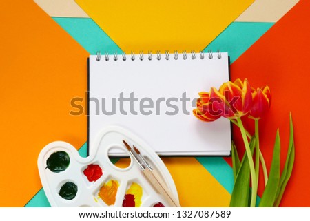 Spring Flat lay. album for drawing, a bouquet of red tulips flowers, paints on a geometrical multi-colored bright background.Spring mood. top view, copy space