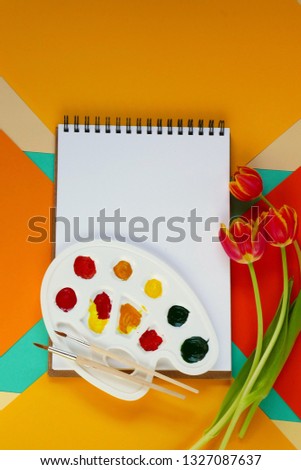 Spring Flat lay. album for drawing, a bouquet of red tulips flowers, paints on a geometrical multi-colored  background.Spring mood. top view, copy space