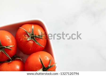 Tomatoes in a white bowl against a marble counter and white background