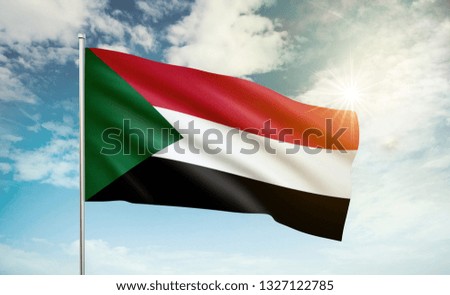Sudan flag waving in the wind against a blue sky and clouds