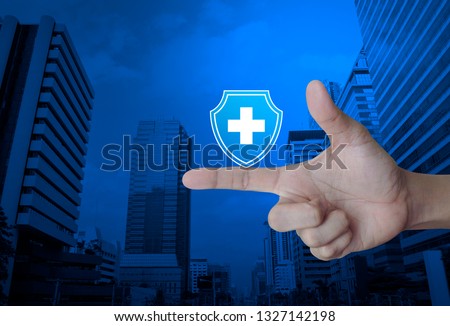 Cross shape with shield flat icon on finger over modern office city tower and skyscraper, Business healthy and medical care insurance concept