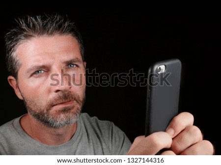 close up face portrait of young attractive and confident white man with blue eyes  using online dating app or internet social media on mobile phone isolated black background in communication concept