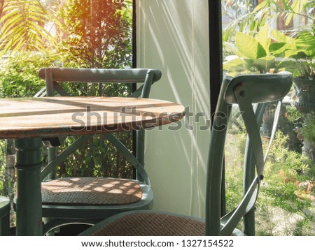 Close-up vintage wooden table and green chair in the corner of restaurant with window glass near the garden.