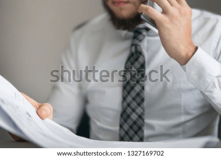 Office work with a laptop. Light background. Holding smartphone in hand. Businessman work with computer on table in office work. Young bearded businessman. Financial business.