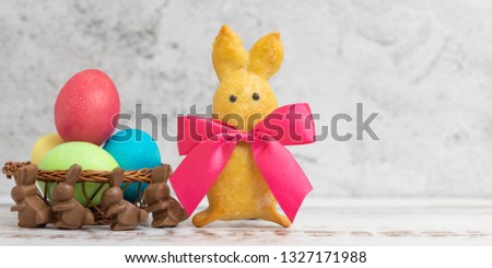 Homemade rabbit-shaped cookies with a red bow and Easter eggs on a light background.