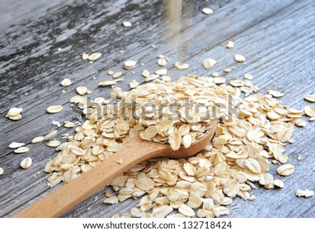 Oat flakes spilling in a wooden spoon on old wooden background