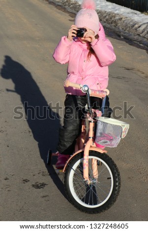 girl in a pink jacket on a bicycle in the spring with a camera