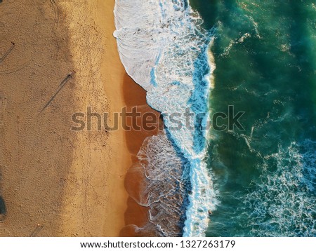 Aerial view of sandy beach with waves with people walking. Drone Shot