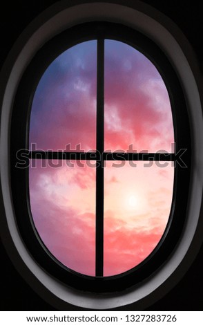 view of pink and purple clouds through the oval window in a dark room