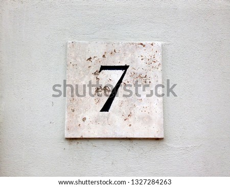 House number 7: textured square sign on white wall