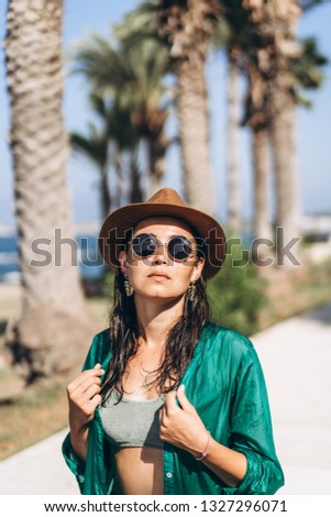 Cute pan asian girl in hat and sunglasses in green pareo walking on the seaside