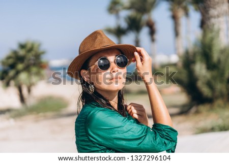 Cute pan asian girl in hat and sunglasses in green pareo walking on the seaside