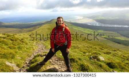 Hiker on a mountain in the Dingle Peninsula with green landscapes, Ireland.