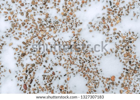 Various colored large group of small stones under the snow during the natural daylight. Close up pattern and texture image of contrast between solid, hard ( stones ) and gentle, subtle ( snow )