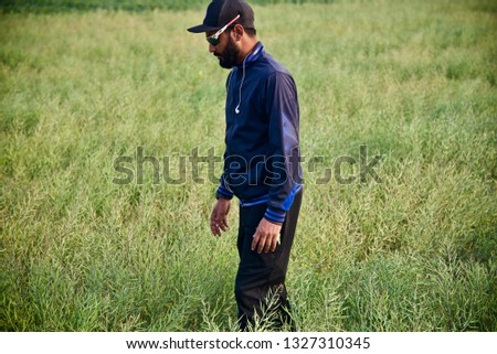 Young man wearing blue jacket standing around a green crops field