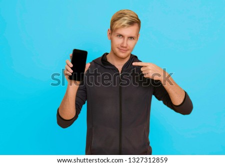 Portrait young man showing mobile phone isolated over blue background.