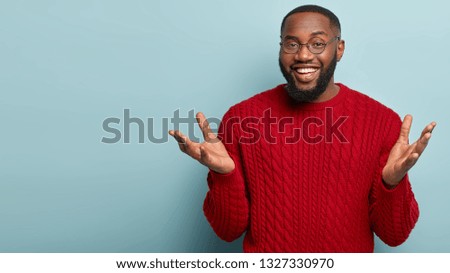 I know nothing. Horizontal shot of friendly looking black man spreads hands, gestures actively while explains something to interlocutor, stands over blue background, mock up space aside, has no idea Royalty-Free Stock Photo #1327330970