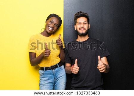 Young interracial couple, indian man and african woman with thumbs up isolated on yellow black background