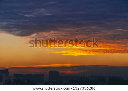 Cityscape with wonderful varicolored fiery dawn. Amazing dramatic multicolored cloudy sky. Dark silhouettes of city building roofs. Atmospheric background of sunrise in overcast weather. Copy space.