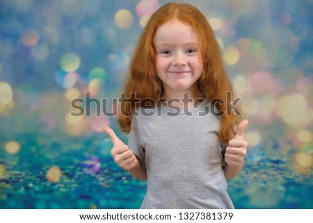 Concept portrait of a cute pretty child girl with red hair on a color background smiling and talking. She stands in front of the camera in a gray T-shirt with different emotions and different poses.
