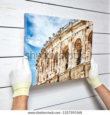 Photography printed on canvas with gallery wrap method of canvas stretching in male hands. Image of architecture of Nimes city, France