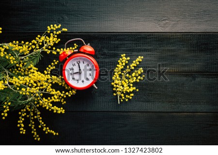 red alarm clock, mimosa twigs, black wooden background, spring morning