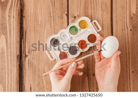 Close-up of woman's hands painting an easter egg on wooden background.