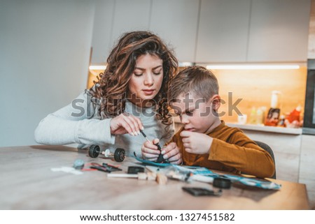 Mom and son concentrate while building a robot. The happy family spends time together at home. Mother helping son with electronic project