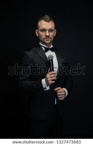 Charismatic host in a black tuxedo on a black background.