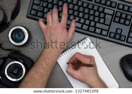 The journalist is working on an article in the office at the computer. Top view of the table with a keyboard, mouse, reflex camera and lens.