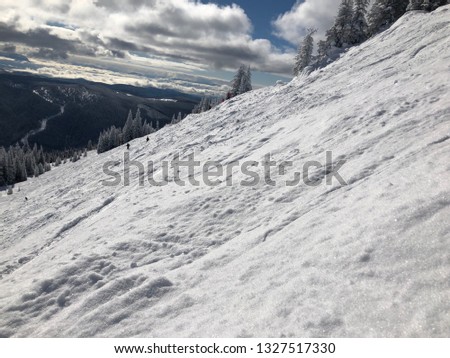 Steep mountain recently skied with landscape of mountain forest and blue sky with white pillowy clouds.