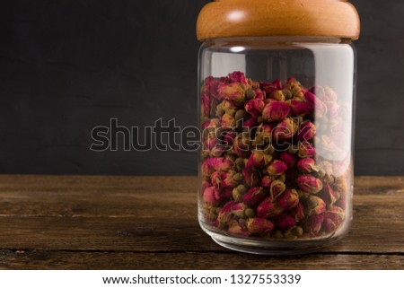 tea rose buds in the transparent jar isolated on the wooden table on black background