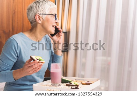 Profile image of beautiful senior woman having healthy meal in her apartment and talking on a mobile phone