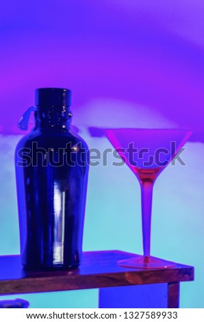 A bottle of alcohol and a cocktail glass on the restaurant table in the beautiful purple-neon light of the bar, close-up