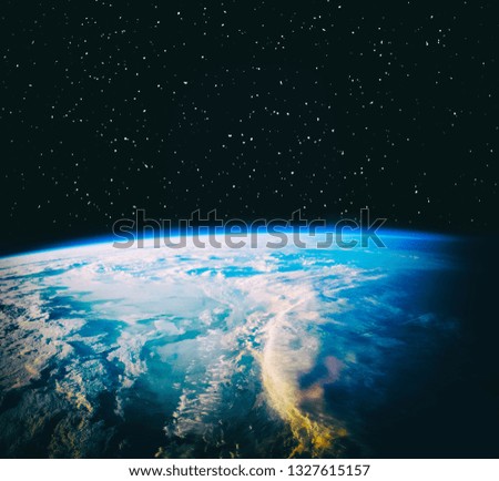 Earth view from space. Clouds and glow above. Stars and galaxy in the distance. Elements of this image furnished by NASA.