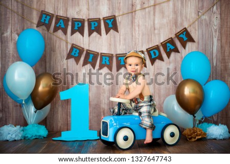 Little boy kid gentleman in retro costume with suspenders and cap is sitting on a wooden car. Children's party with balloons Happy Birthday, 1 year