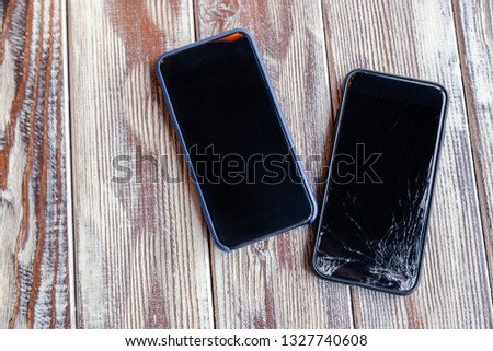 Сloseup black smartphone no brand with a broken screen glass lying on wooden table. Concept of dropping phone, broken gadget, electronics repair, bad luck, credit, unforeseen expenses