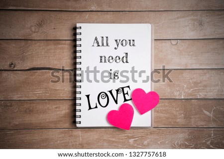 All you need is love quote on a notepad with 2 hearts on wooden background. Flat lay or top view